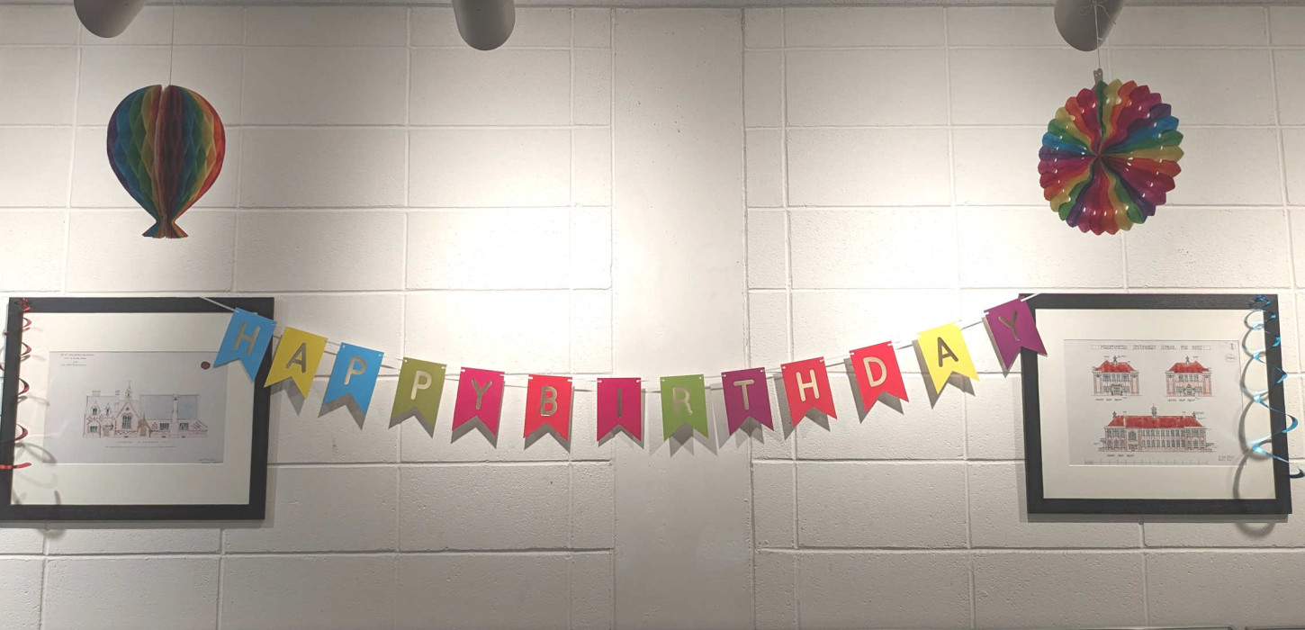 Happy Birthday banner and paper decorations hang on a wall with two prints